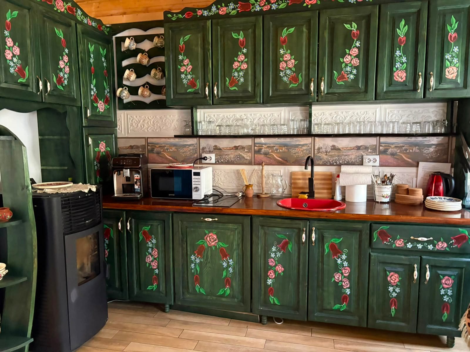 Bucătăria interioară a casei — mobilier verde pictat manual cu trandafiri și lalele, blat de lemn și chiuvetă roșie